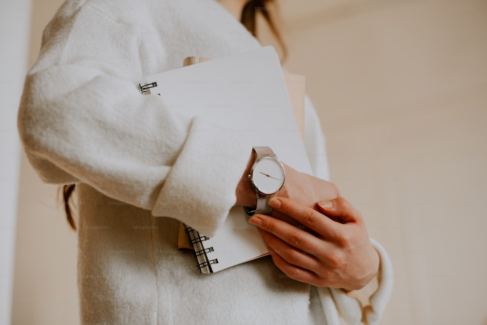 a woman in a white coat holding a notebook and a watch
