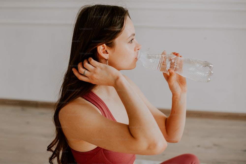 a woman sitting on the floor drinking a bottle of water