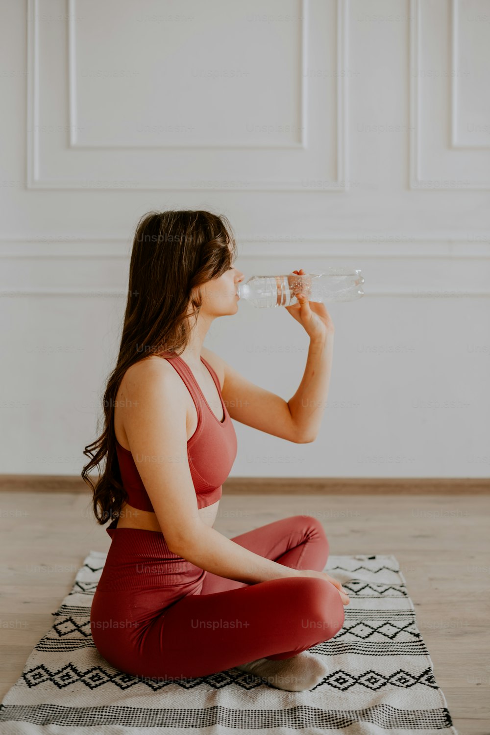 a woman sitting on a rug drinking water