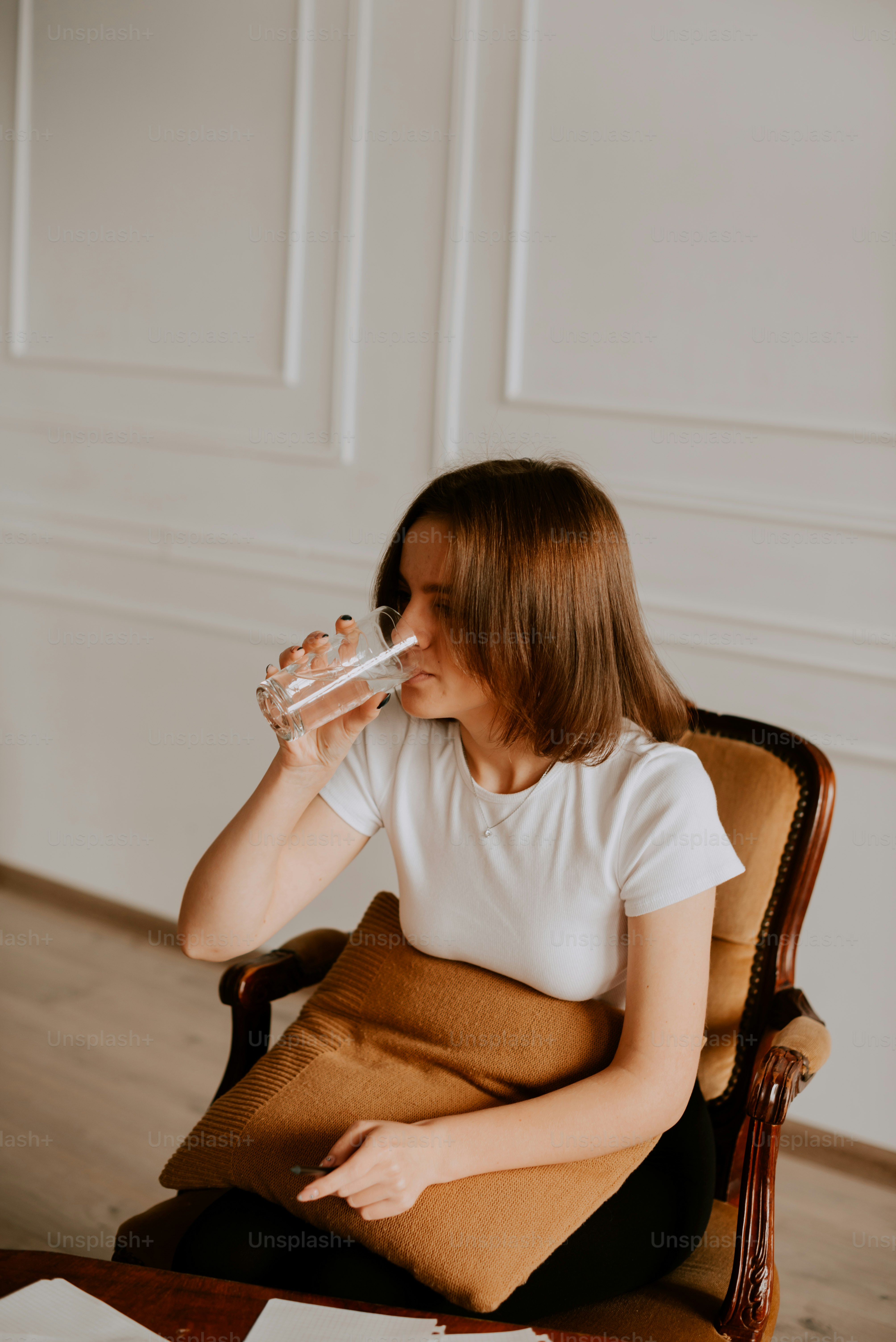 une femme assise sur une chaise buvant un verre d’eau