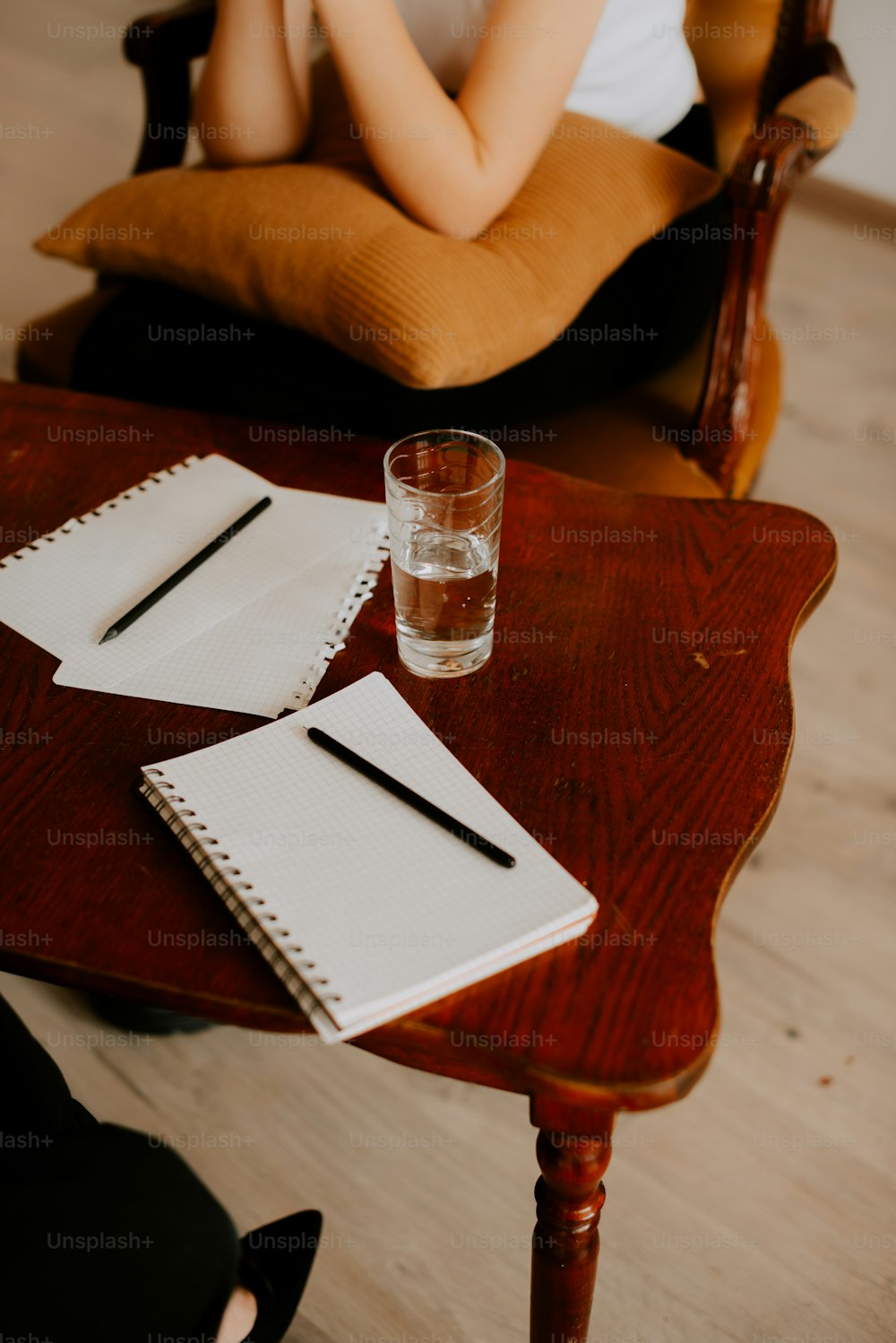 a wooden table topped with a notebook and a glass of water