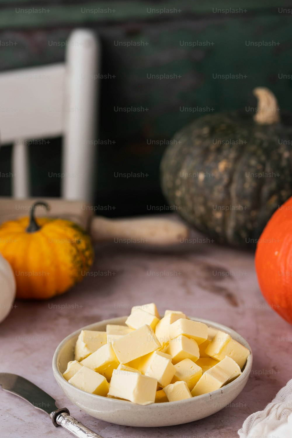 a bowl of butter sits on a table next to pumpkins