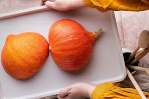 a person holding a tray with two oranges on it