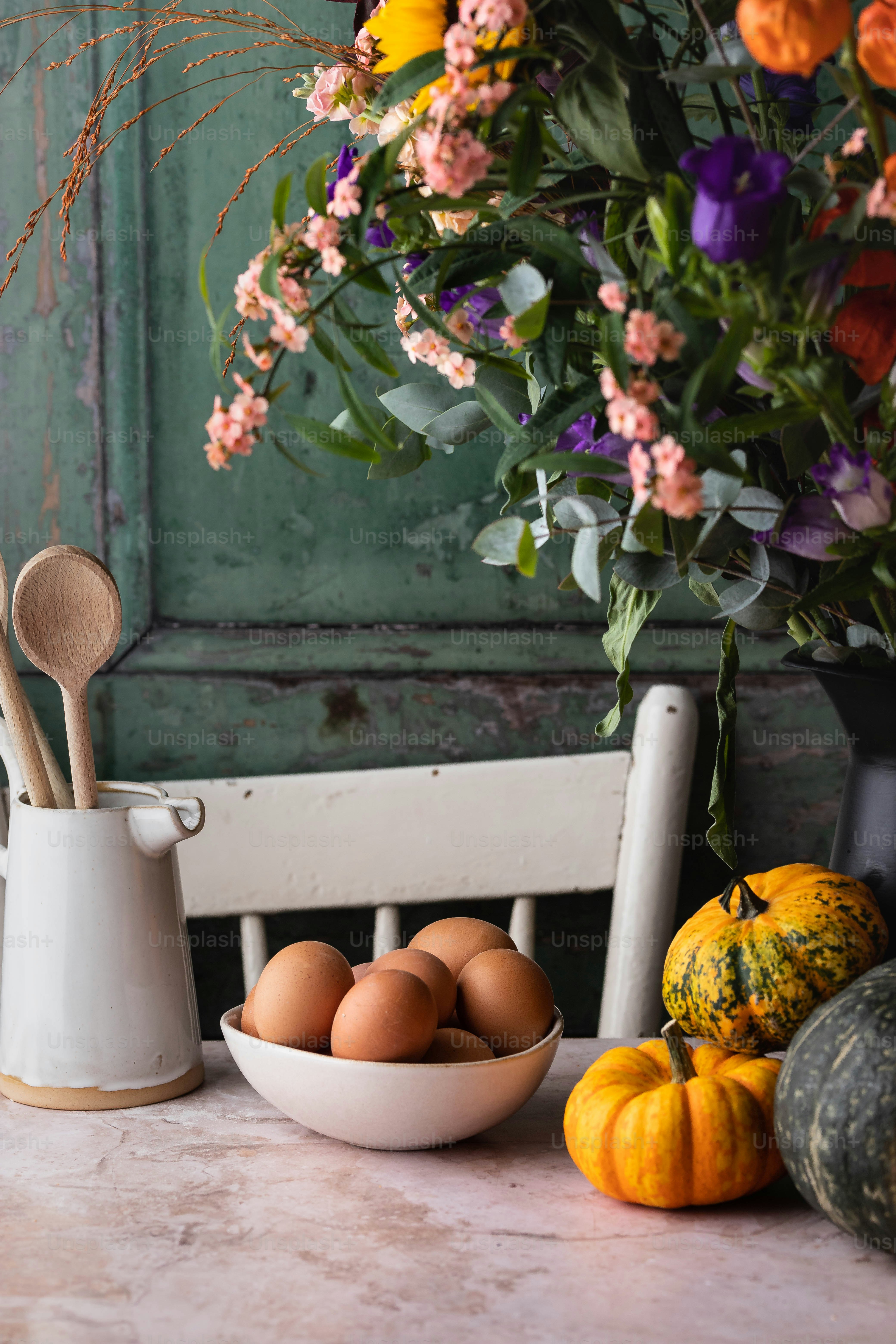 una ciotola di uova seduta su un tavolo accanto a un vaso di fiori