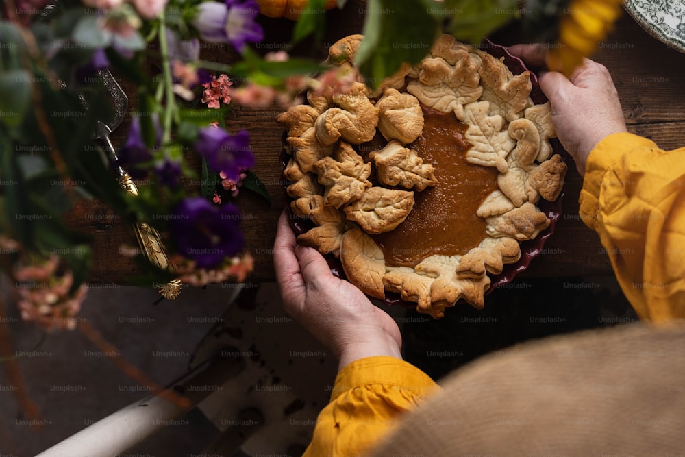 a person holding a pie on top of a wooden table