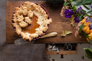 a pie sitting on top of a wooden table next to flowers