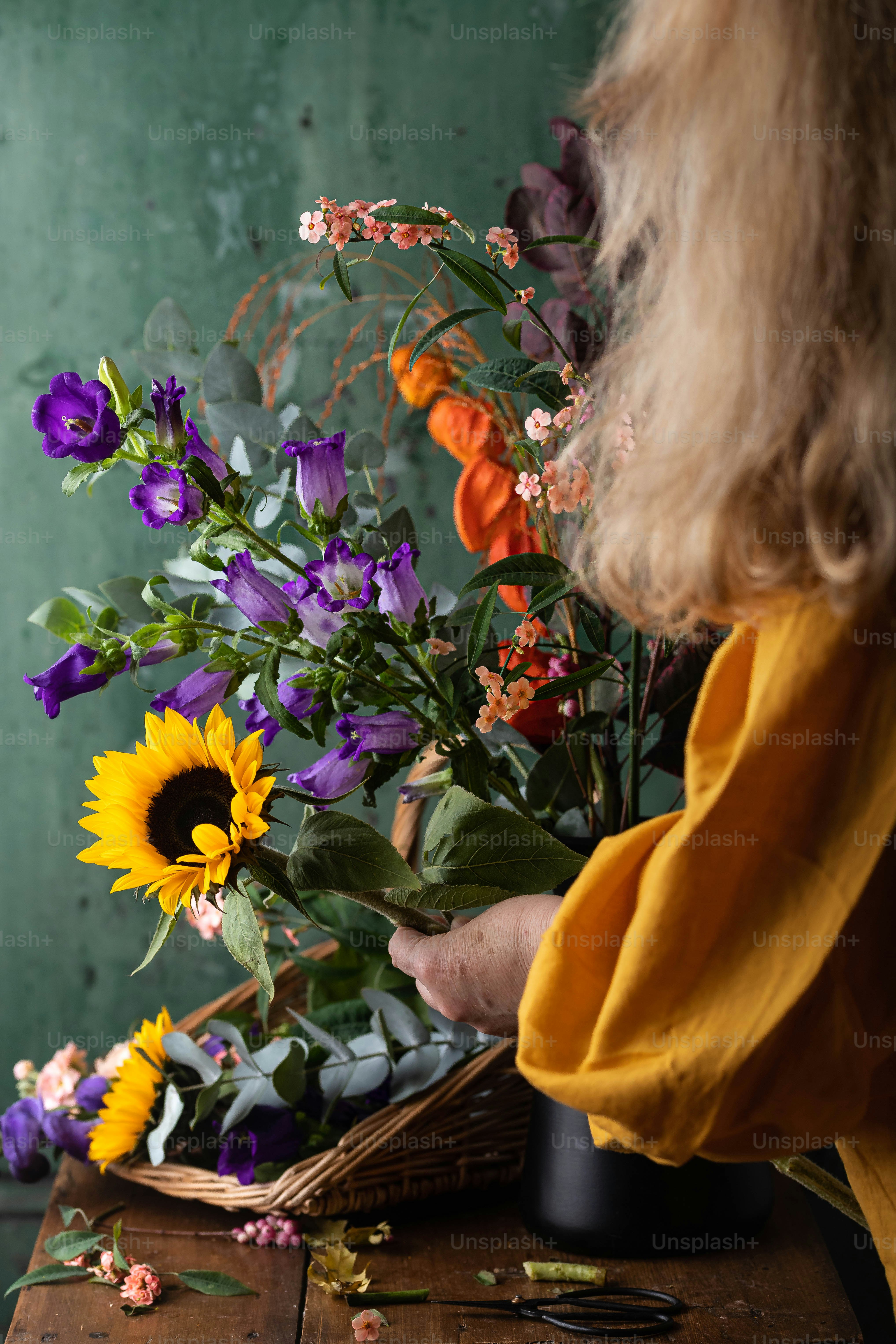 a woman arranging flowers in a basket on a table