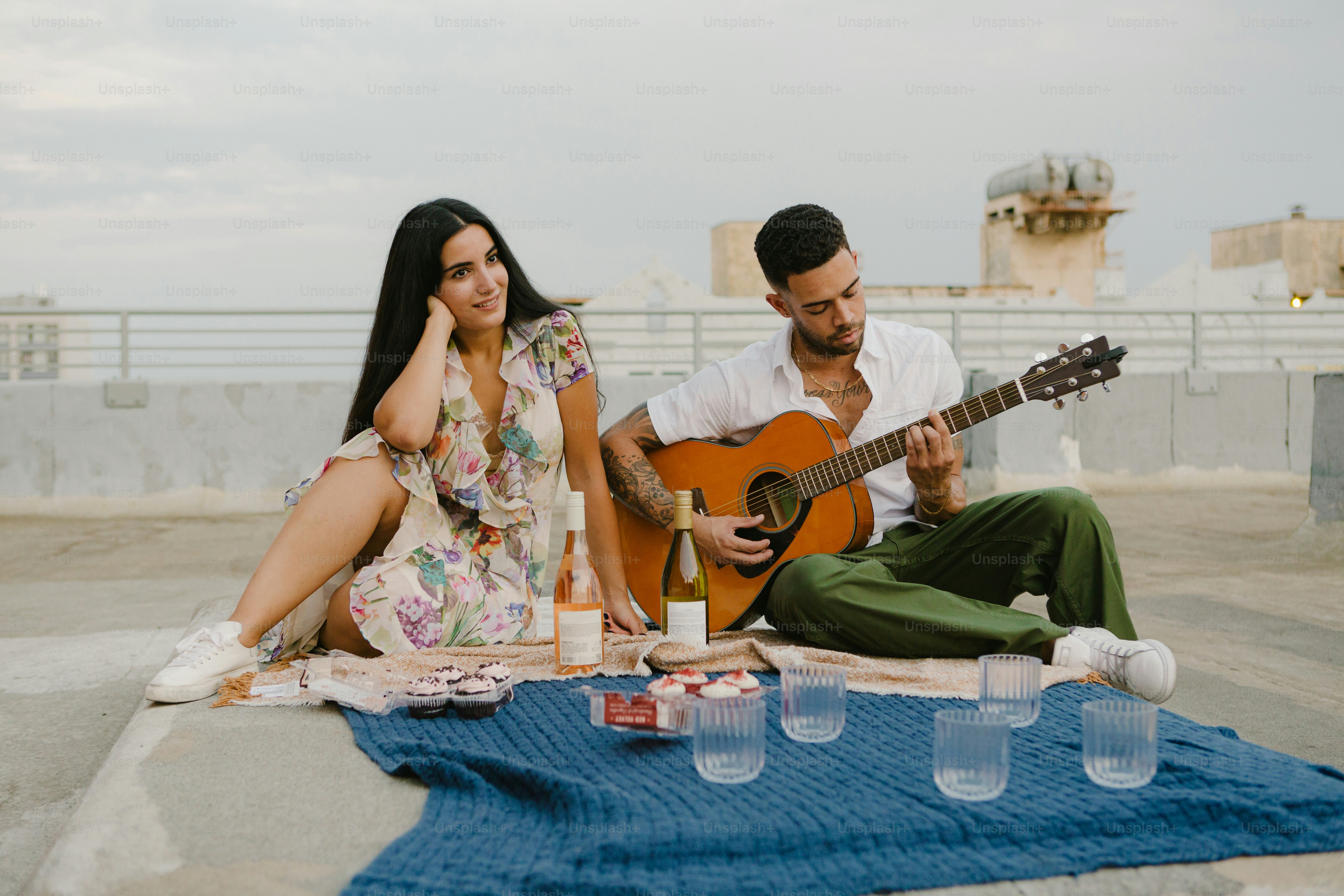 a man and a woman sitting on a blanket playing a guitar