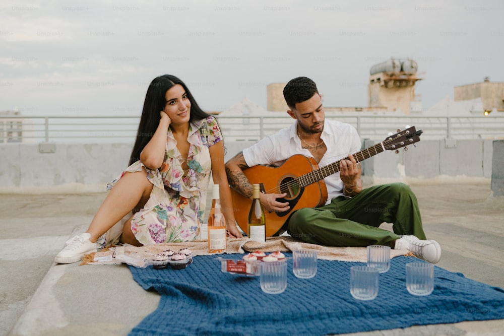 a man and a woman sitting on a blanket playing a guitar