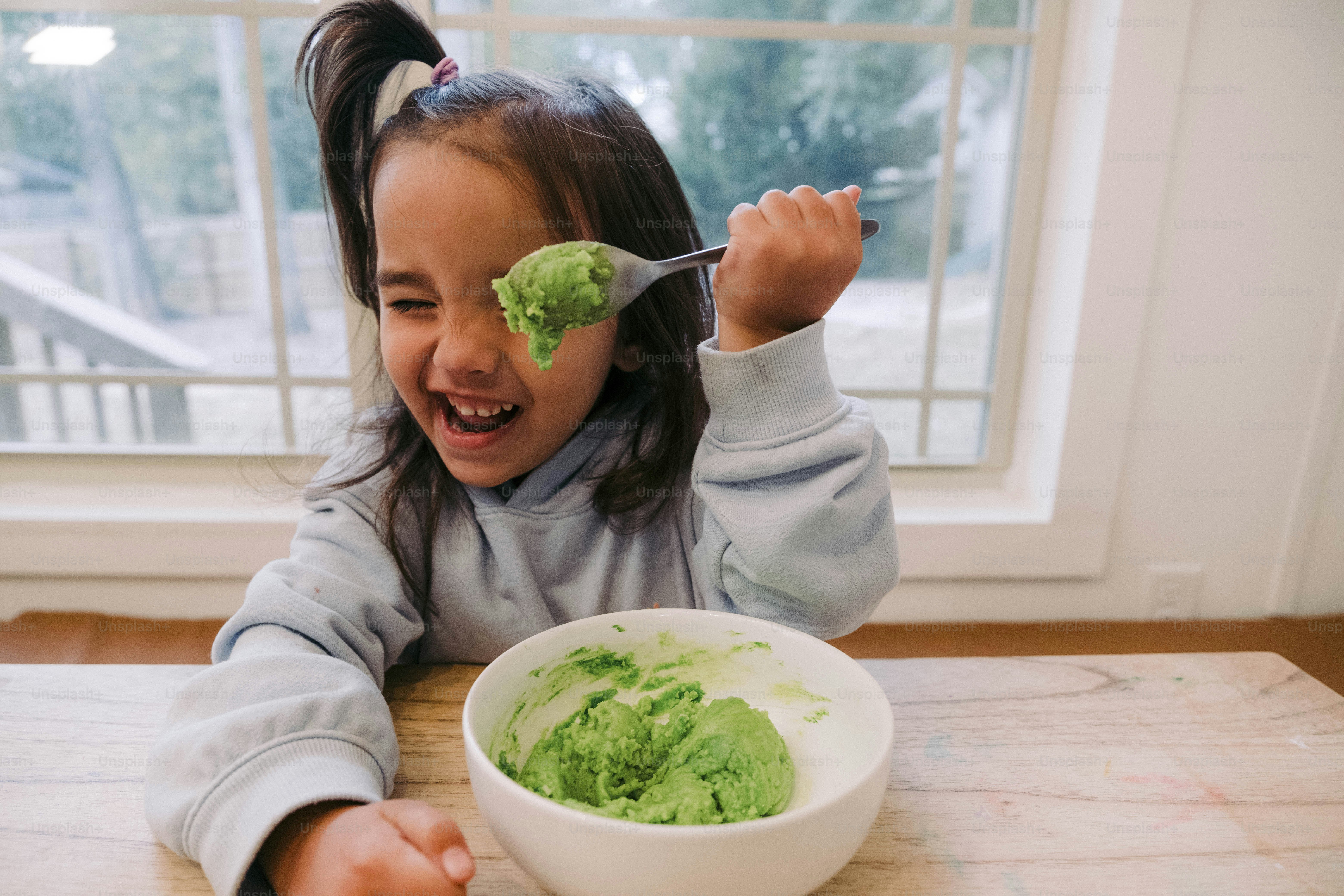 a young girl eating a bowl of green food