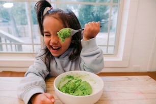 a young girl eating a bowl of green food