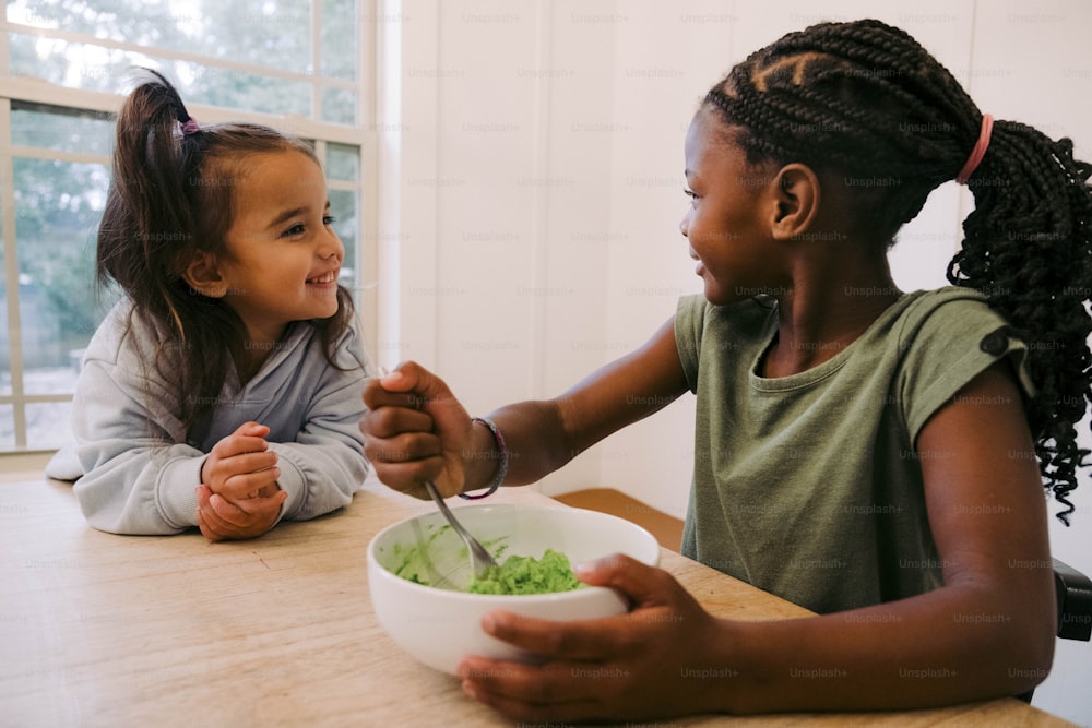 two young girls sitting at a table with a bowl of food