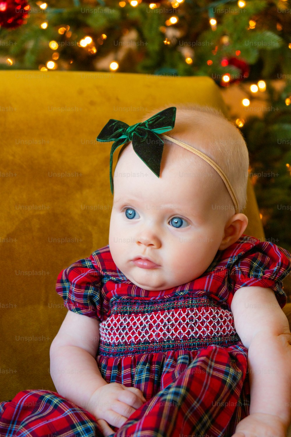 a baby sitting on a chair in front of a christmas tree