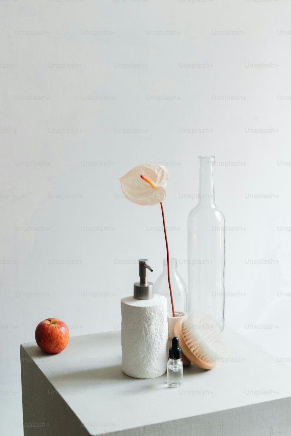 Una bottiglia, un distributore di sapone e una mela siedono su un tavolo