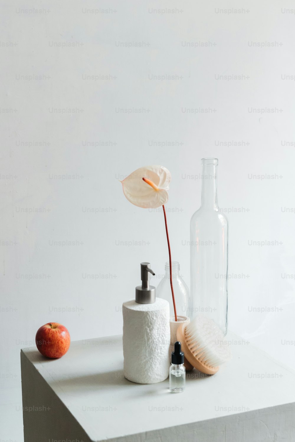 Una botella, un dispensador de jabón y una manzana se sientan sobre una mesa