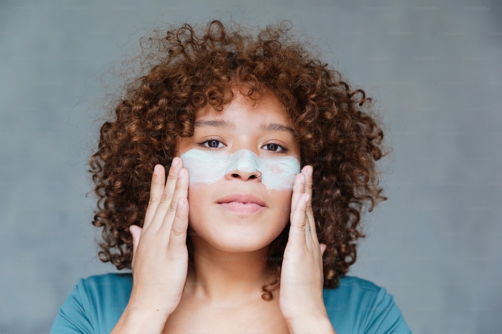 uma mulher levando as mãos ao rosto com muito creme no rosto