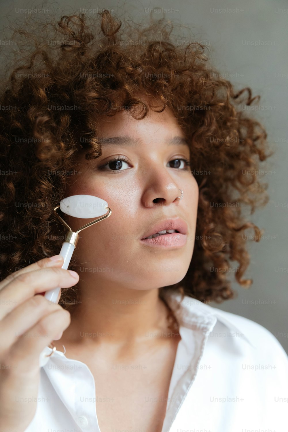 a woman with curly hair brushes her face with a brush