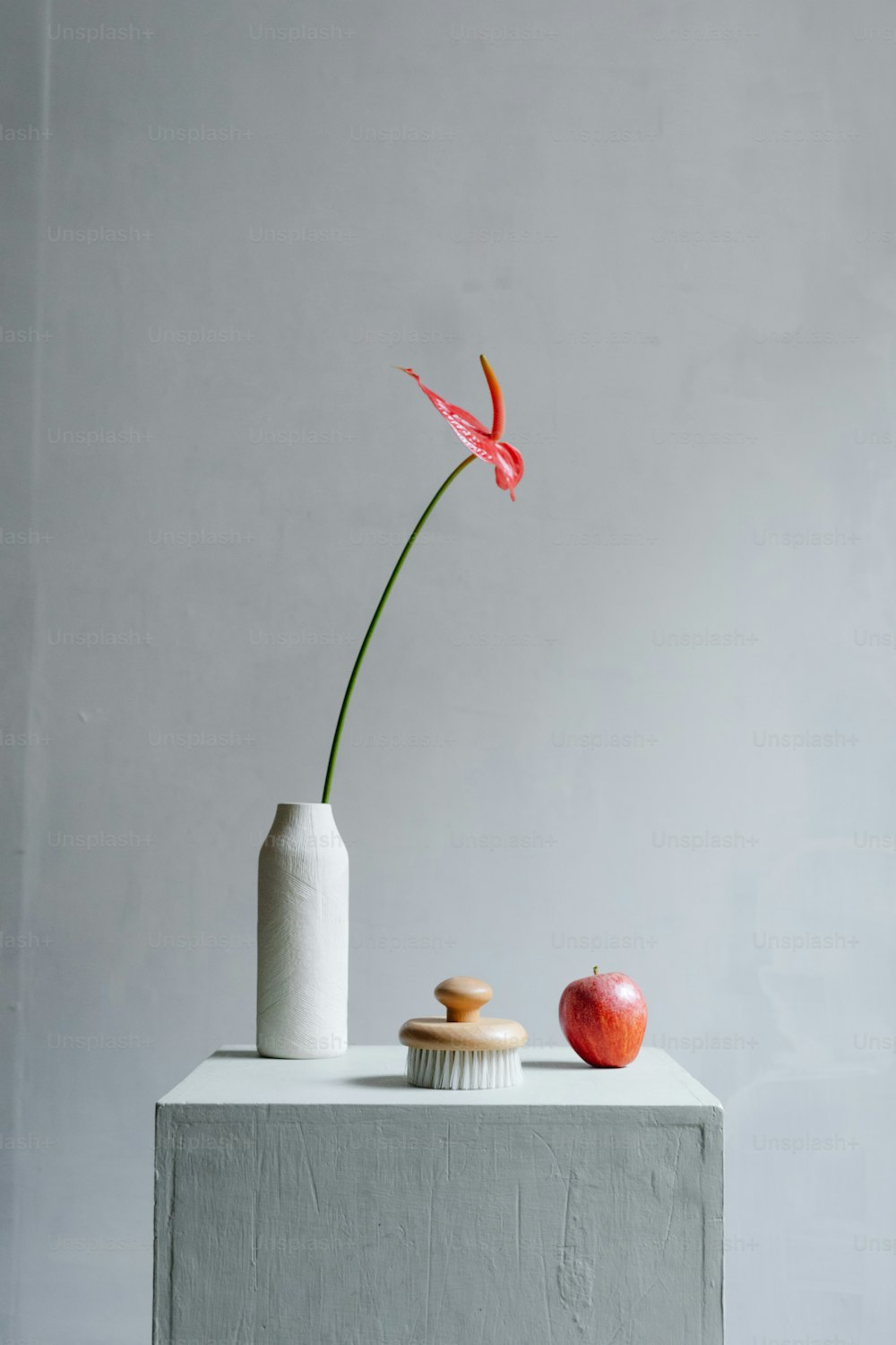 a vase with a flower in it next to an apple