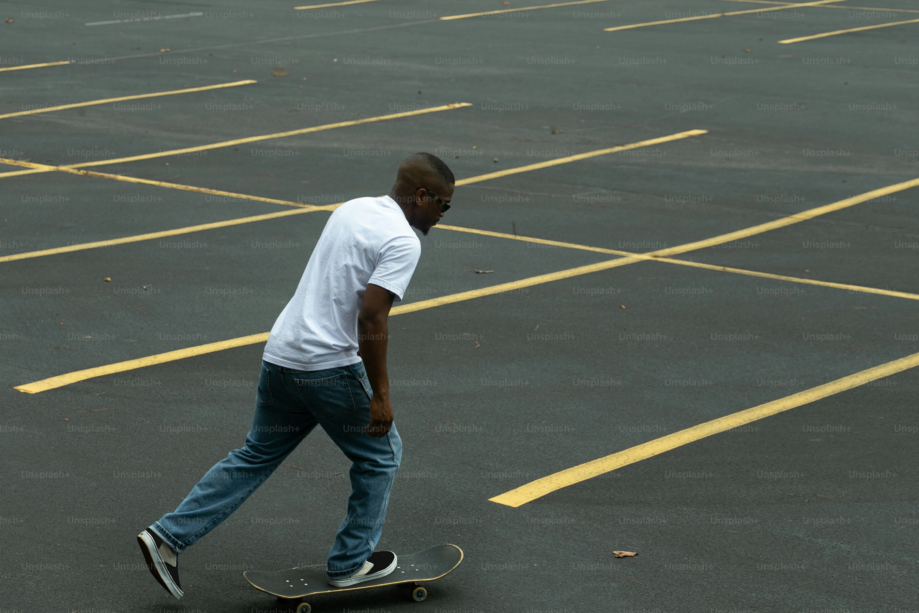 Seorang pria mengendarai skateboard melintasi tempat parkir