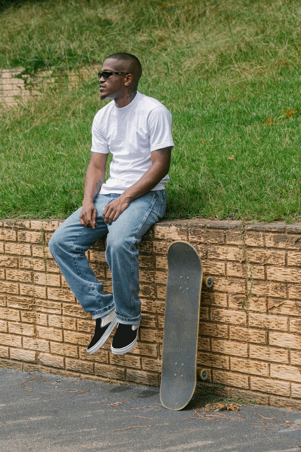 Un uomo seduto su un muro di mattoni con uno skateboard