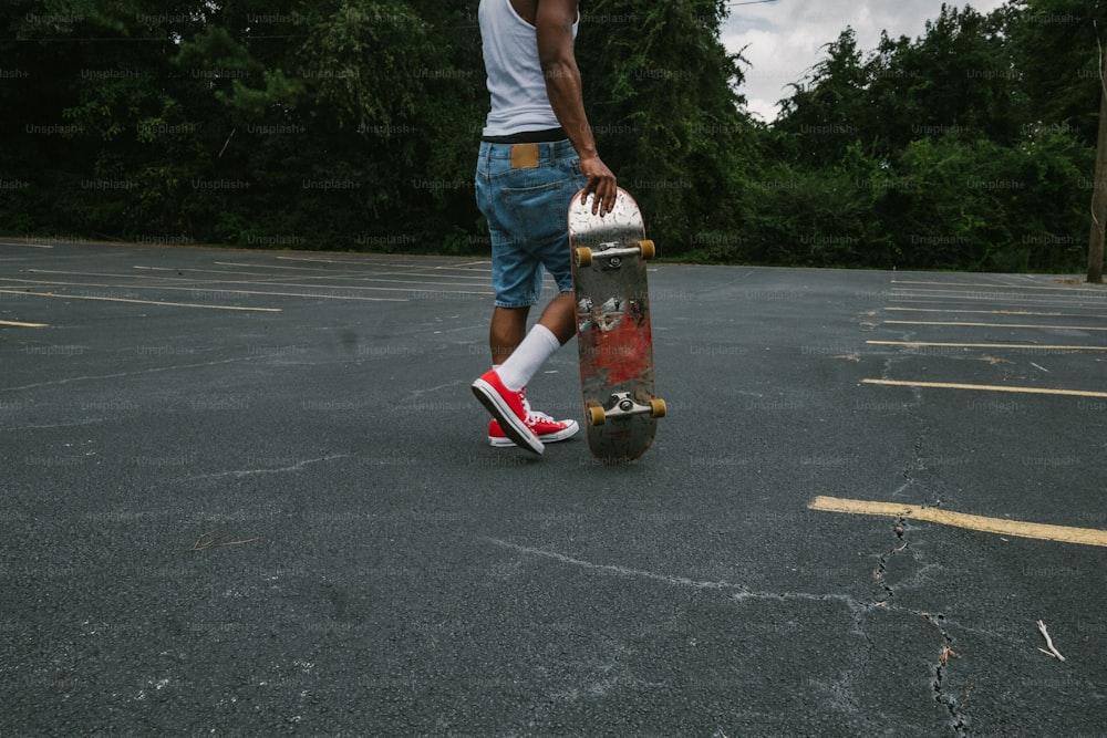 a young man holding a skateboard in a parking lot