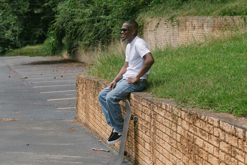 스케이트보드를 들고 벽돌 벽에 앉아 있는 남자