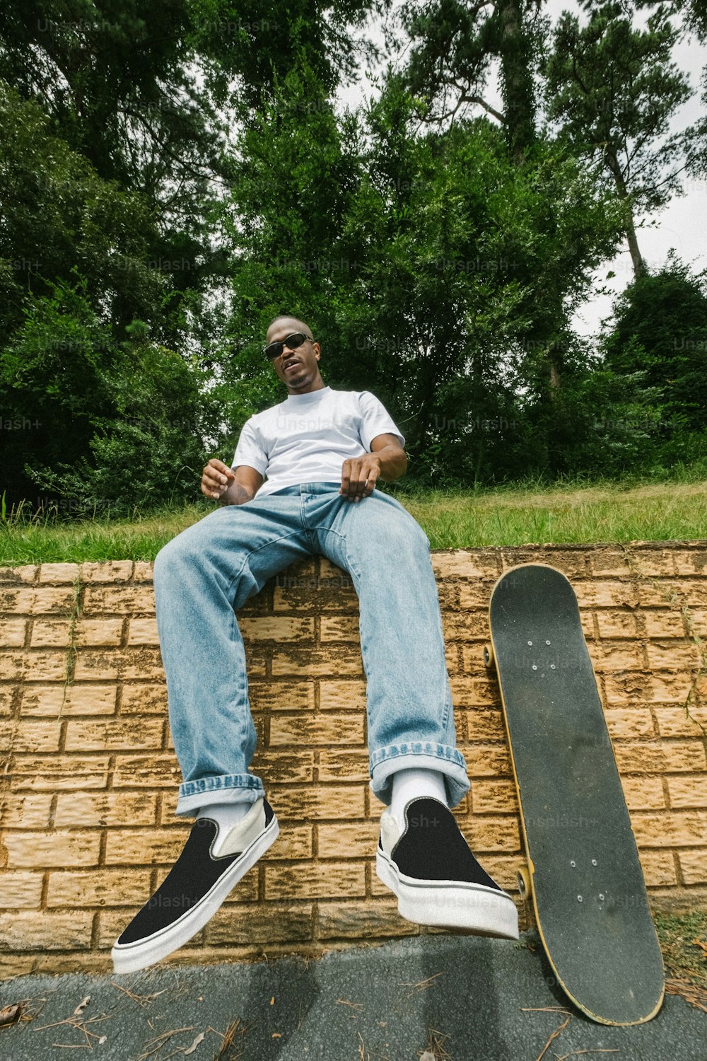 a man sitting on a brick wall next to a skateboard