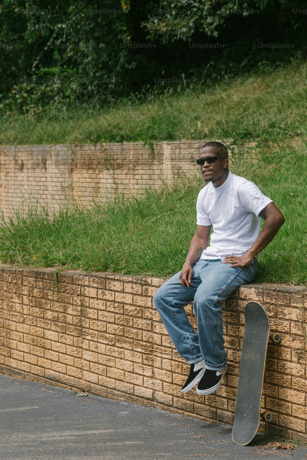 Ein Mann, der mit einem Skateboard auf einer Ziegelmauer sitzt