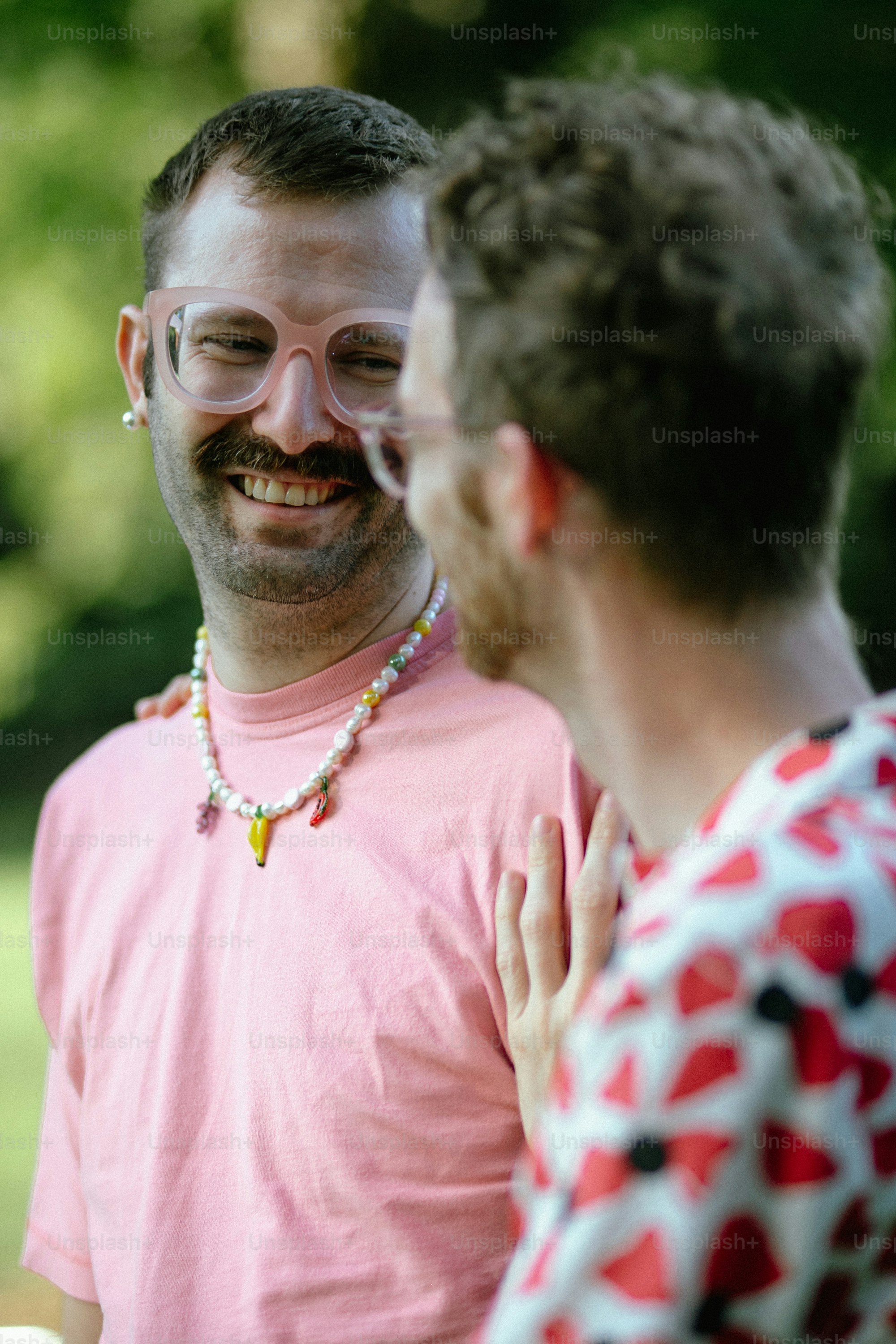 ピンクのシャツを着た男が別の男と話している