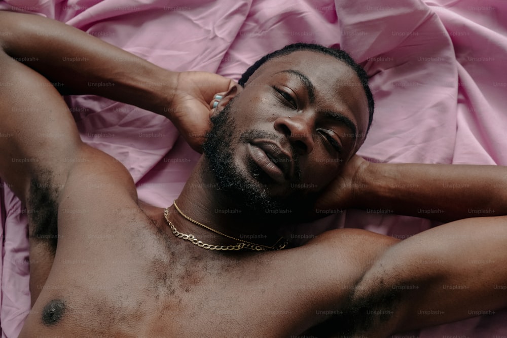 Un uomo a torso nudo che giace su un lenzuolo rosa