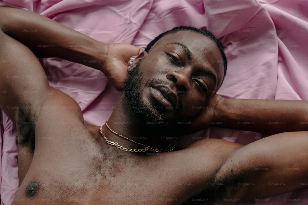 a shirtless man laying on a pink sheet
