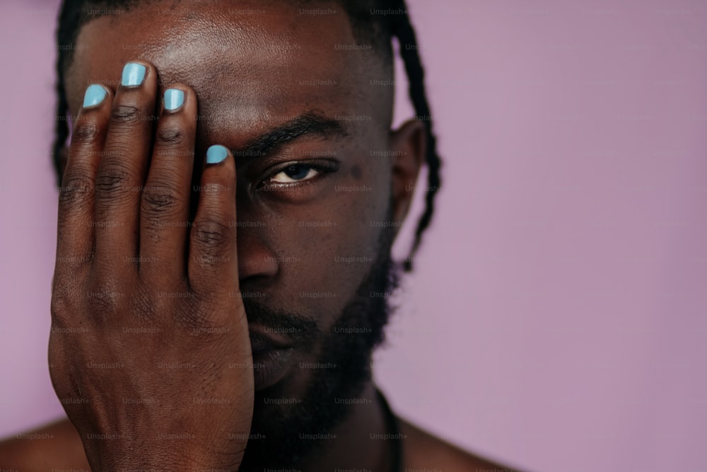 a black man with blue nail polish holding his hands to his face