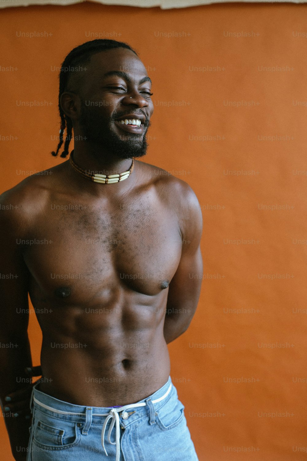 a man with no shirt on standing in front of an orange wall