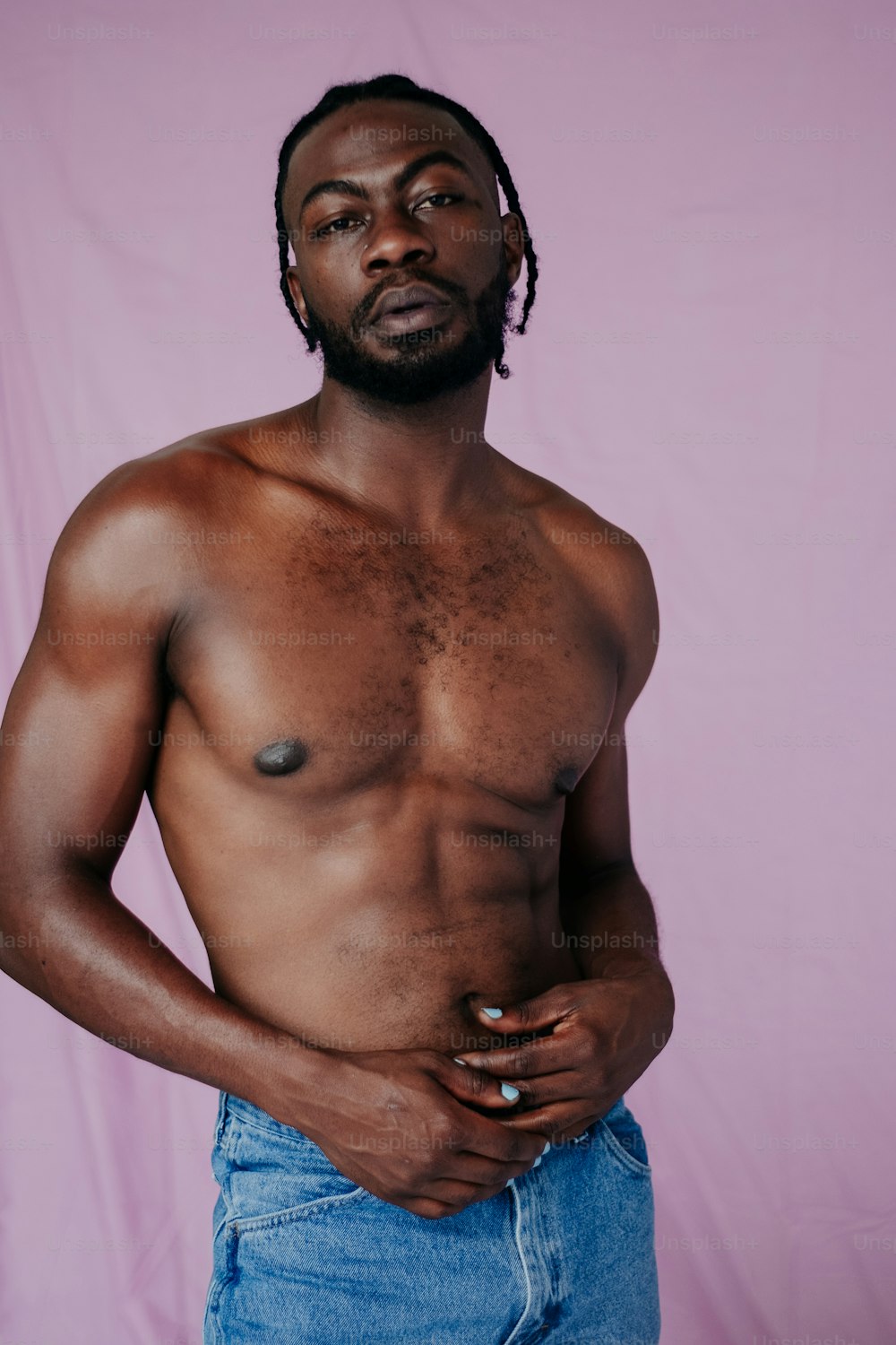 a man with no shirt standing in front of a pink background