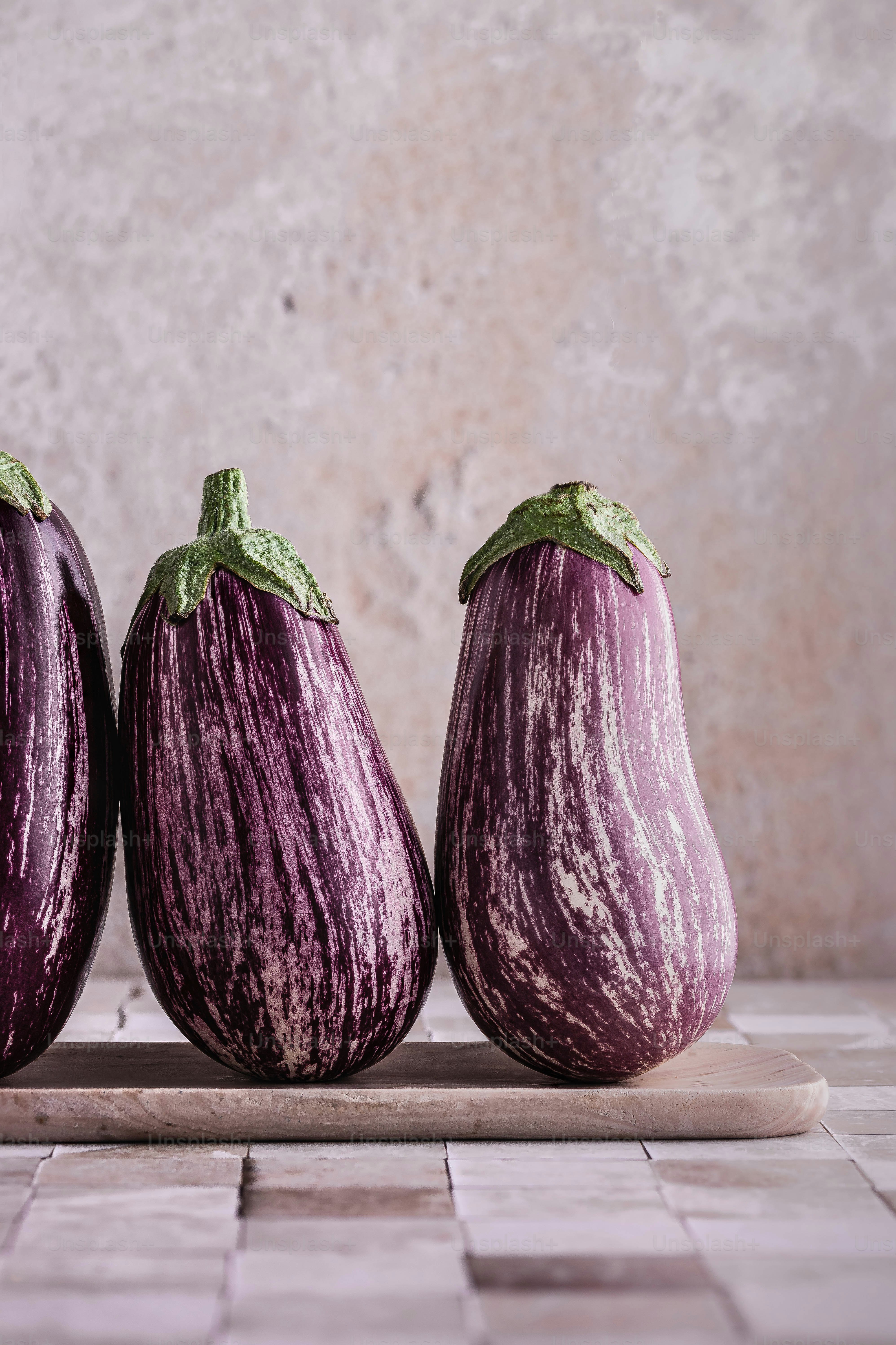drei lila Auberginen, die auf einem hölzernen Schneidebrett sitzen