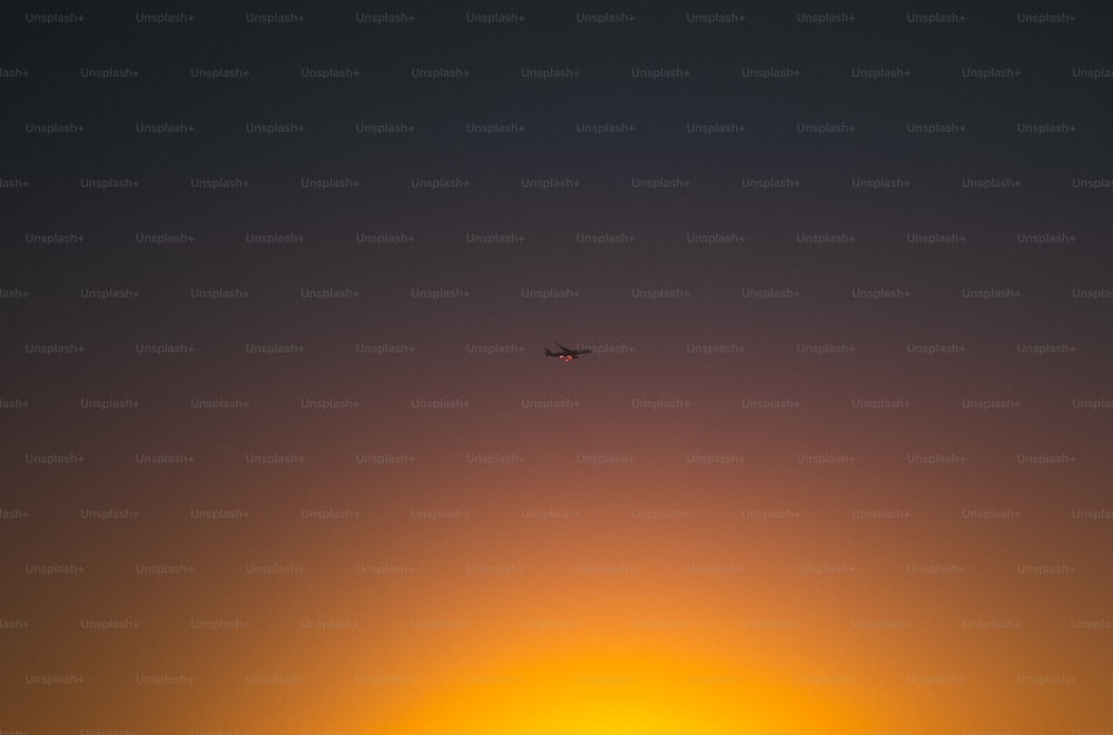 a plane flying in the sky at sunset