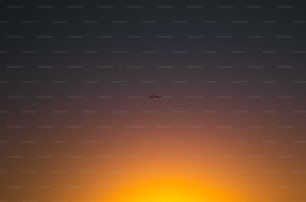 a plane flying in the sky at sunset