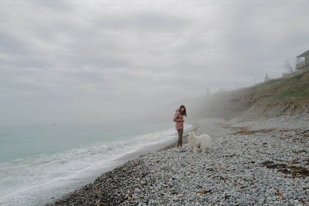 a woman standing on a rocky beach next to a dog