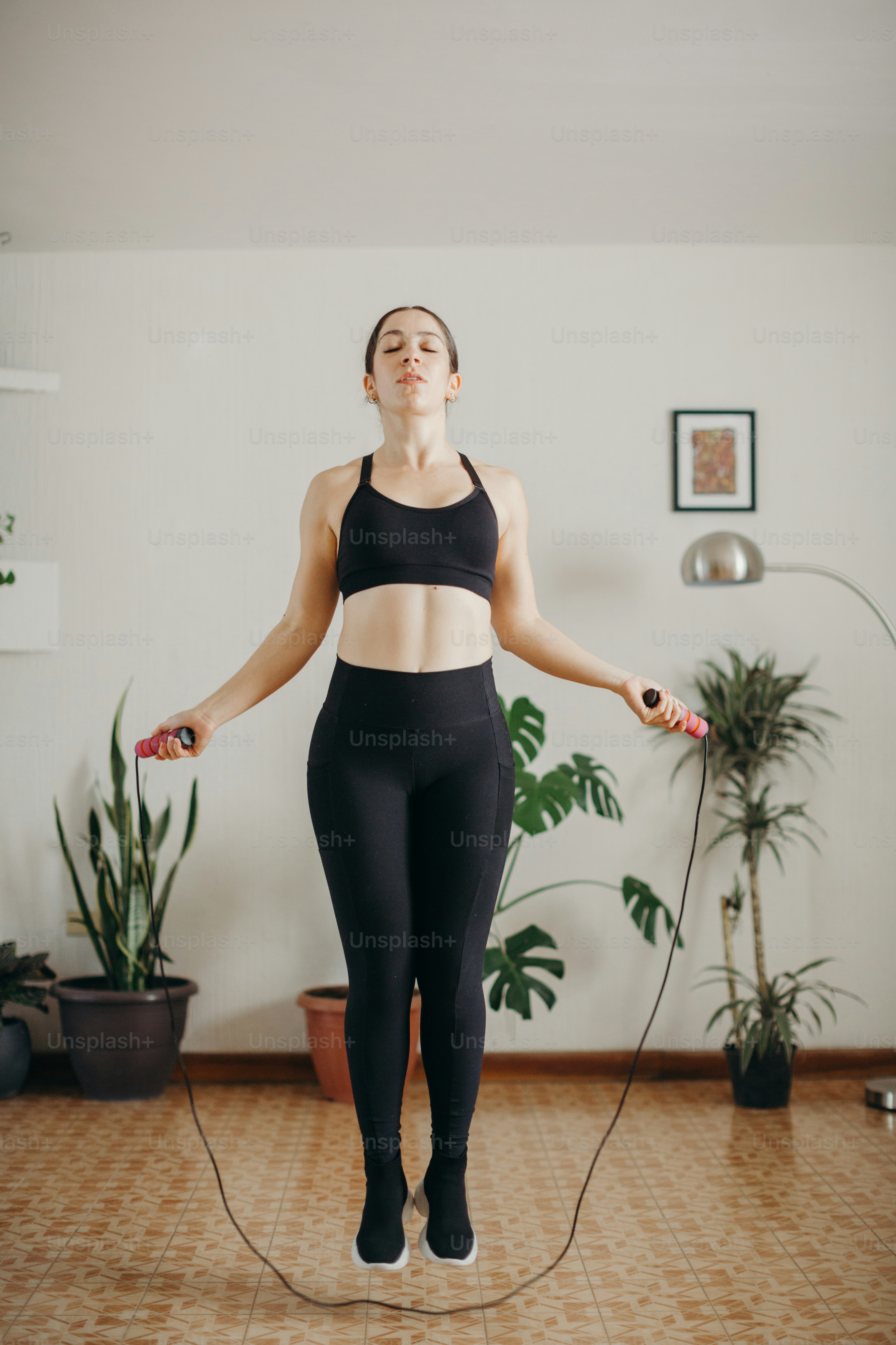 Eine Frau in einem schwarzen Sport-BH-Oberteil und schwarzen Leggings hält einen Sprung