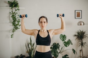 a woman in a black sports bra holding two dumbbells