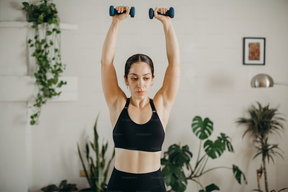a woman in a black sports bra holding two dumbbells