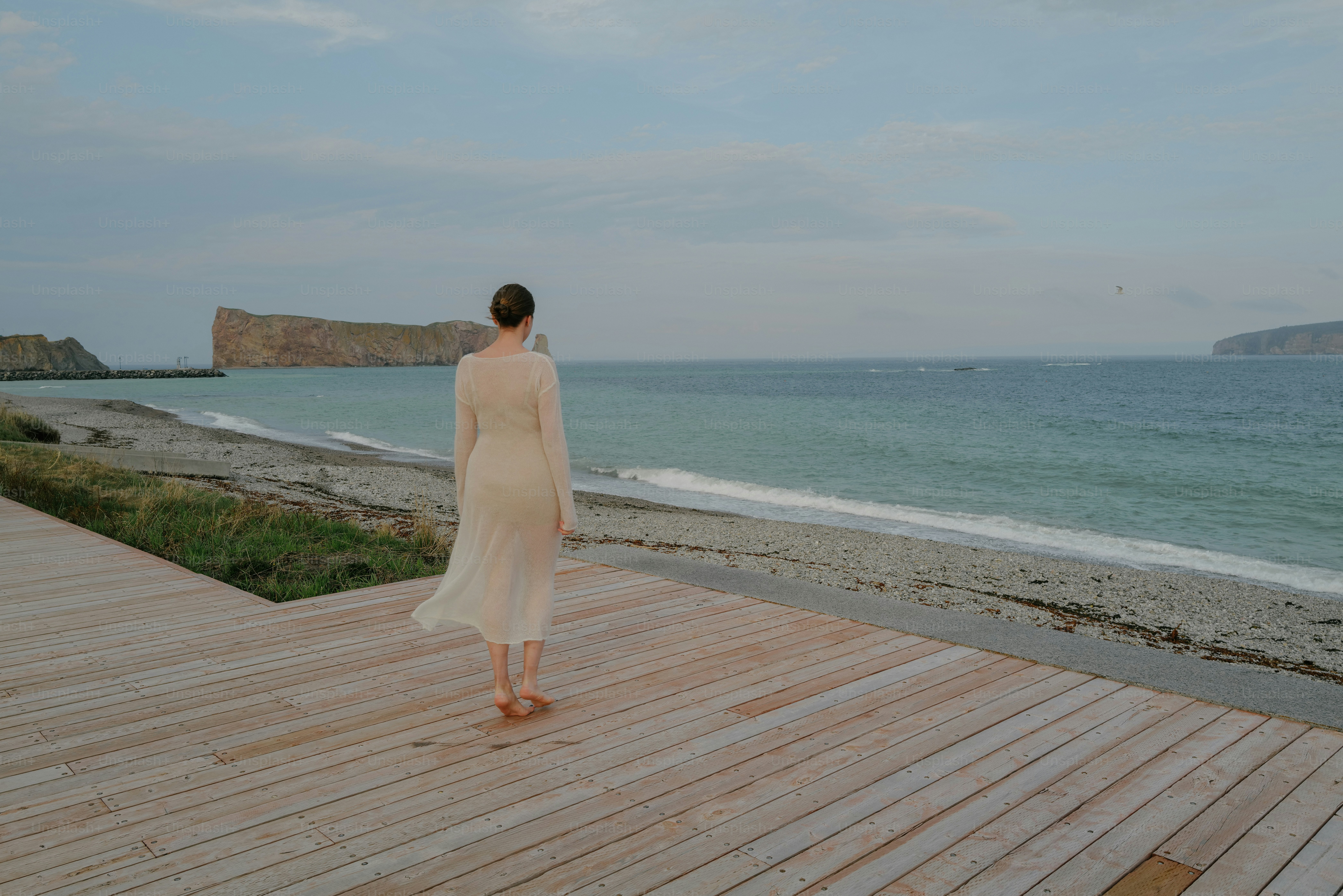 a woman standing on a wooden deck near the ocean