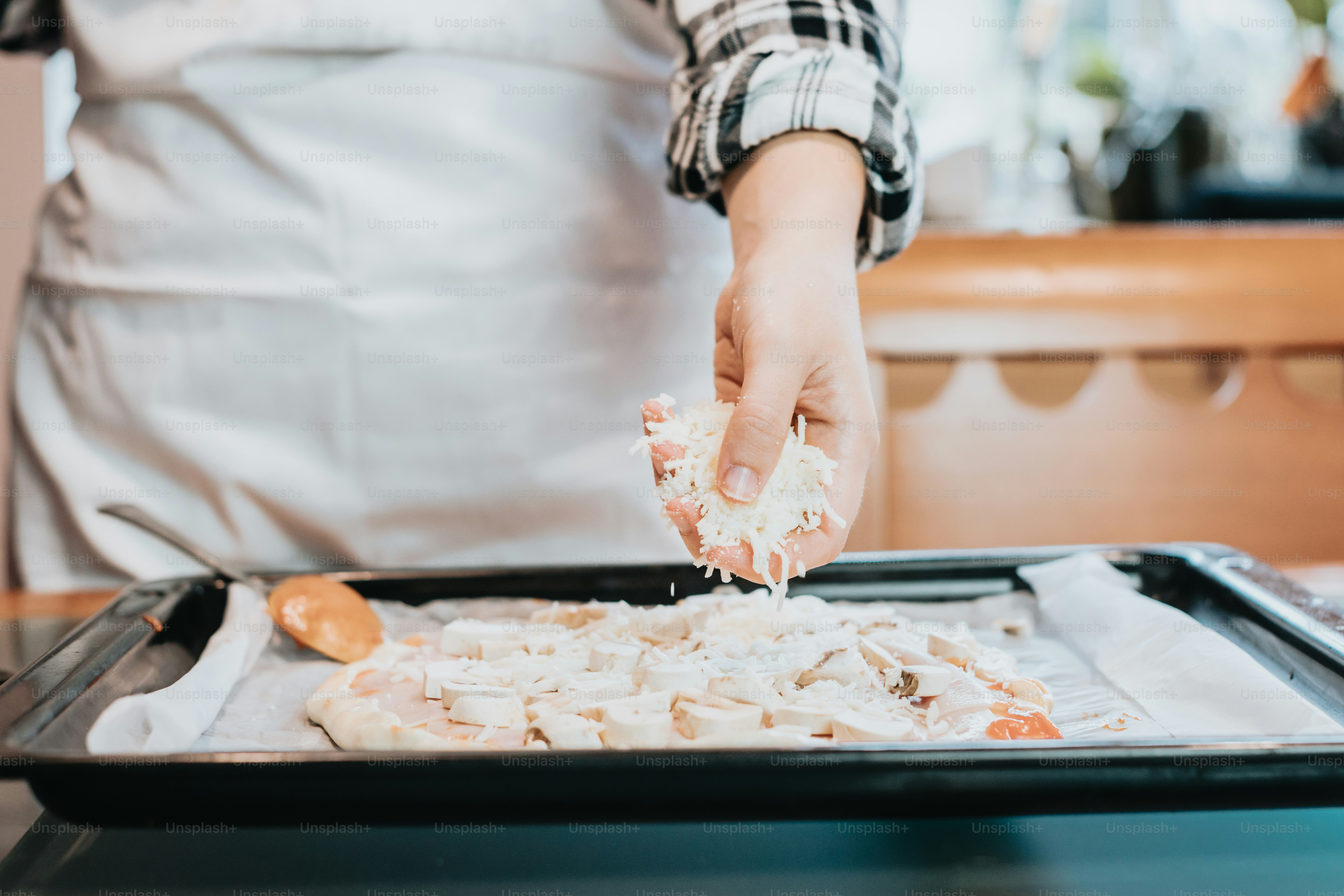 una persona in un grembiule che cosparge di formaggio su una pizza