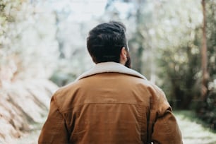 a man in a brown jacket walking through a forest
