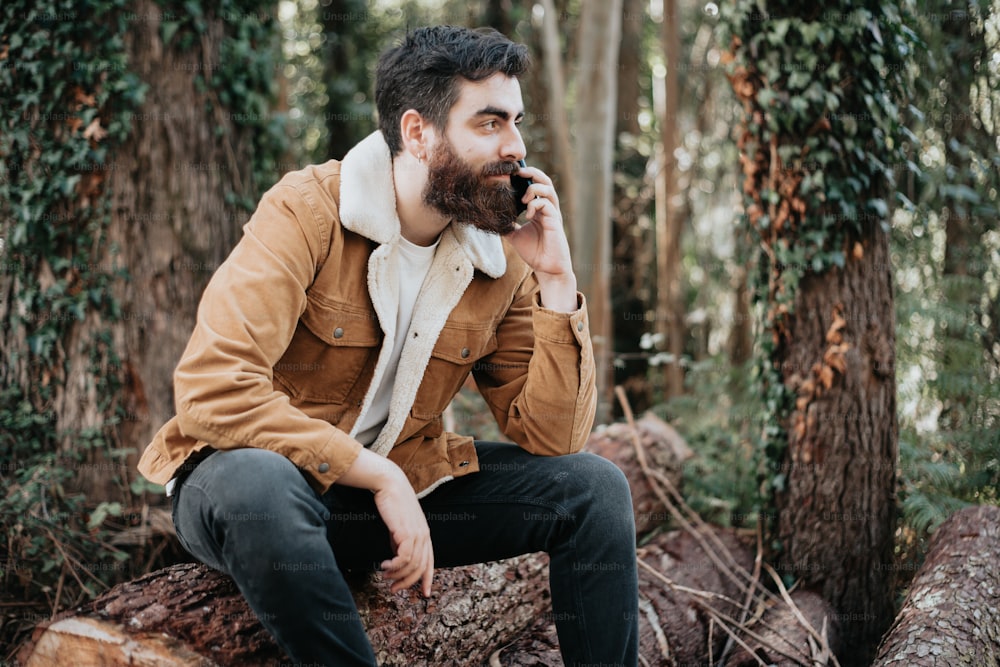 a bearded man sitting on a log in the woods