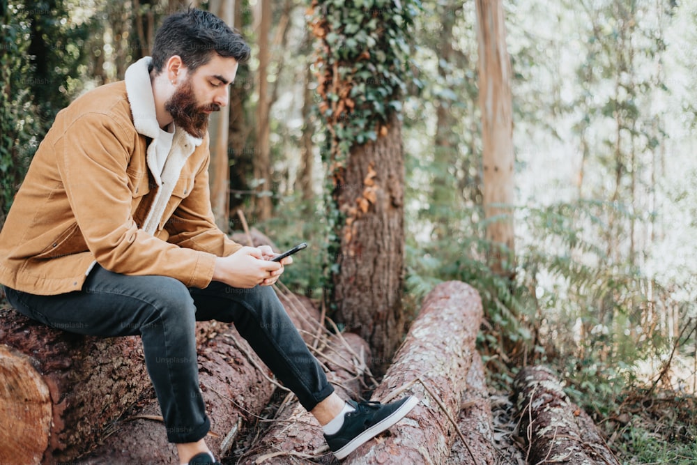 Un hombre sentado en un tronco mirando su teléfono celular