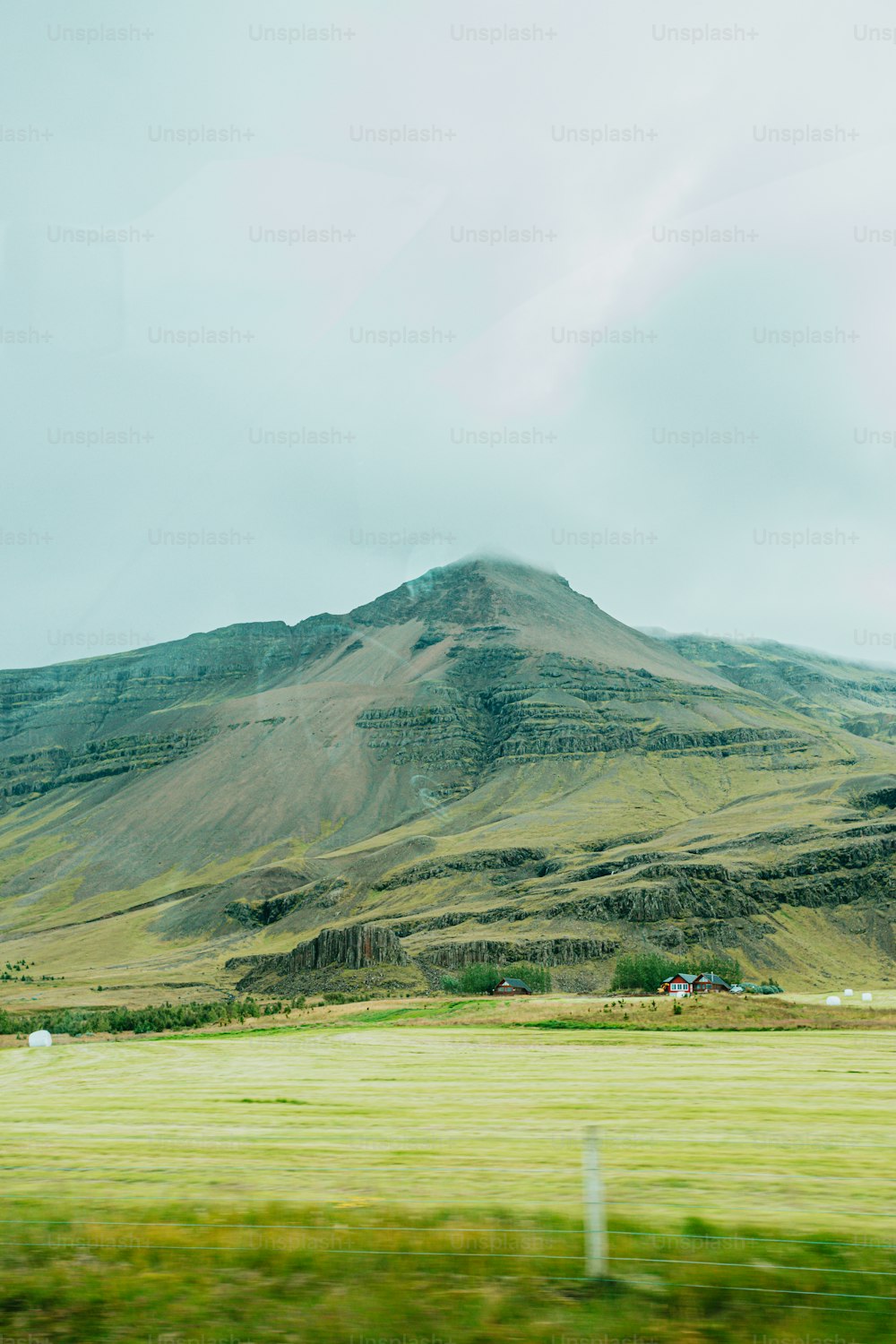 a large mountain with a grassy field below it