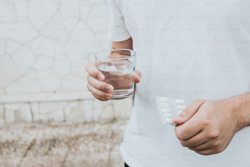 a man holding a glass of water and pills