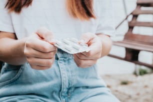 uma mulher sentada em um banco segurando um pacote de comprimidos