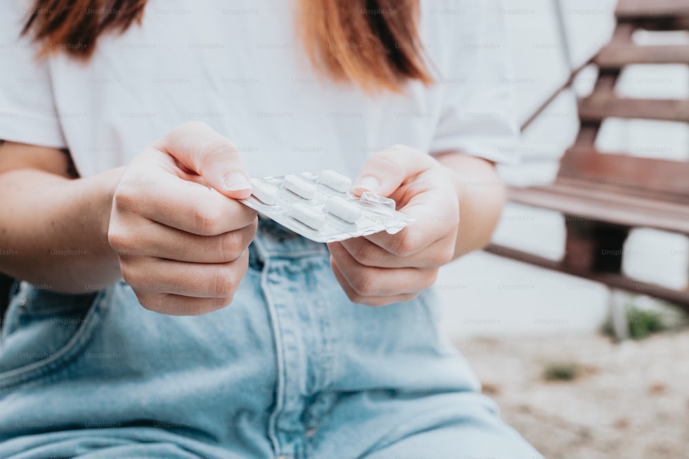 a woman sitting on a bench holding a pack of pills